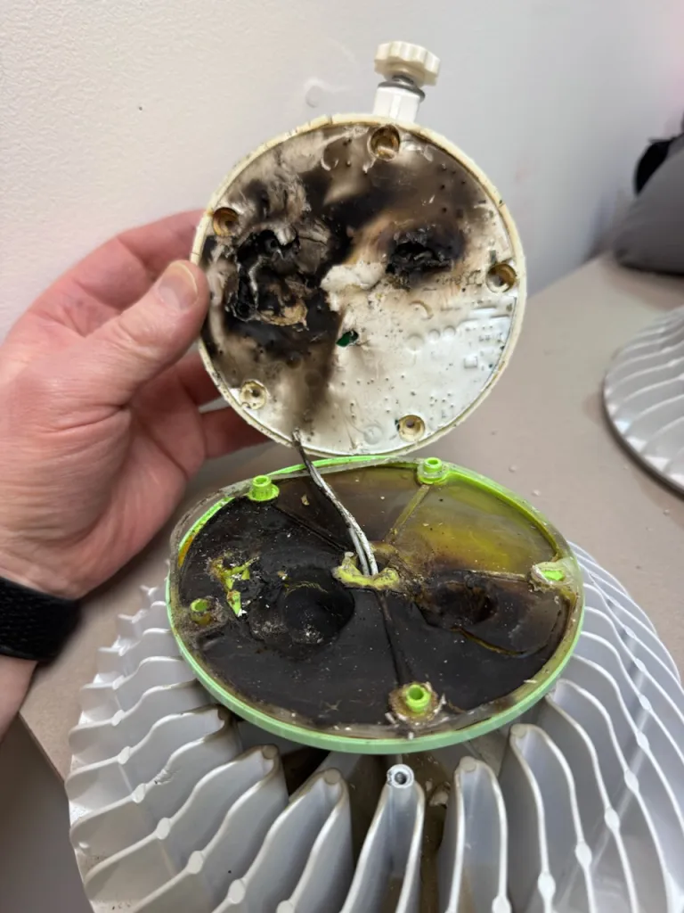 Someone’s hand holds a burnt-out and blackened light bulb.