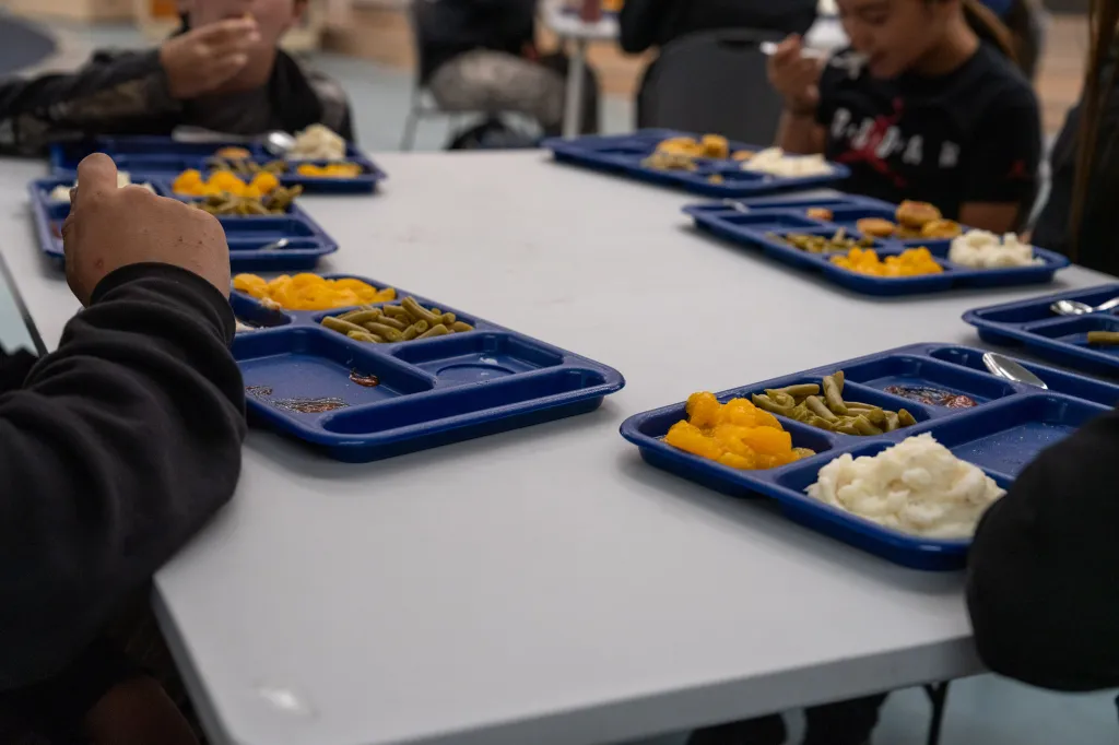 A close-up of kids eating food from lunch trays.