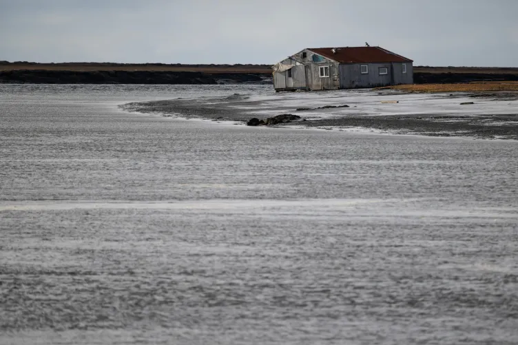 A battered one-story home leans to the side, surrounded by water.