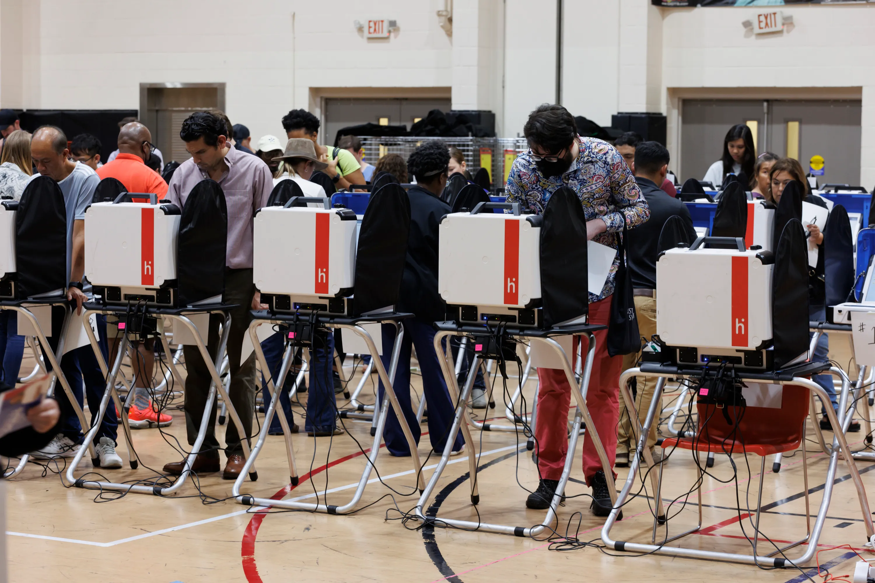 People stand in rows at voting booths inside a gymnasium.