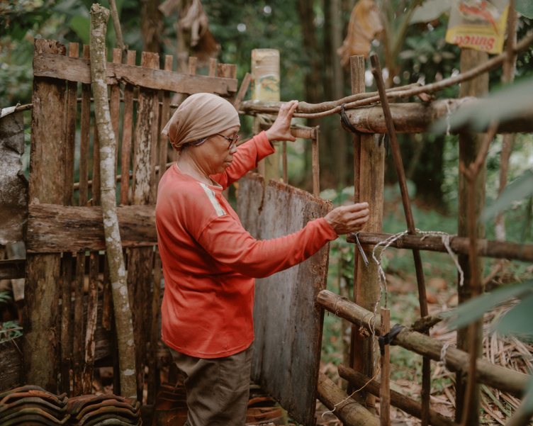 Cicih holds part of a wooden fence. She is surrounded by plants.