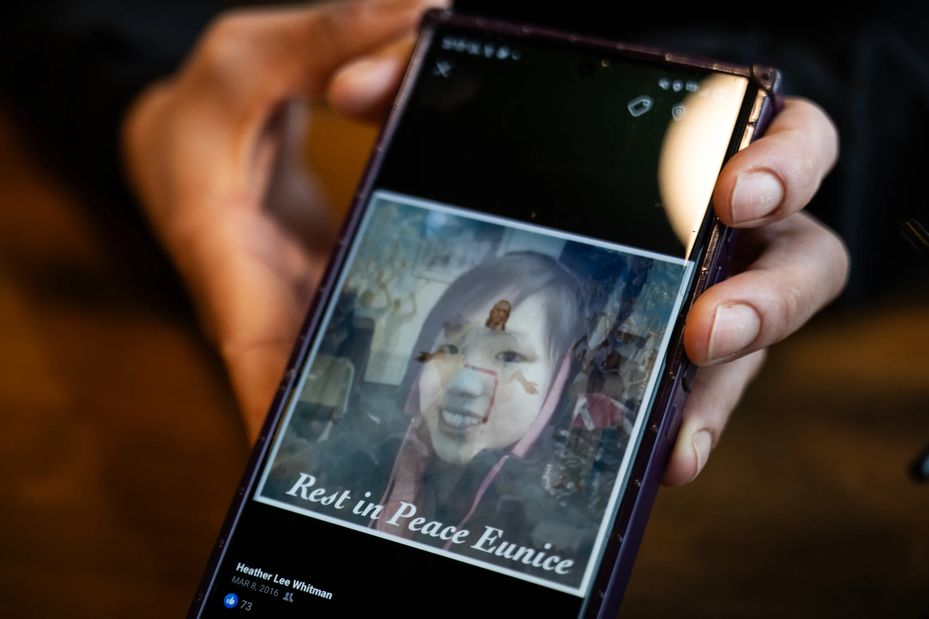 A hand holds a phone with a photo of a smiling girl overlaid with an image of Jesus Christ and the words “Rest in Peace Eunice.”