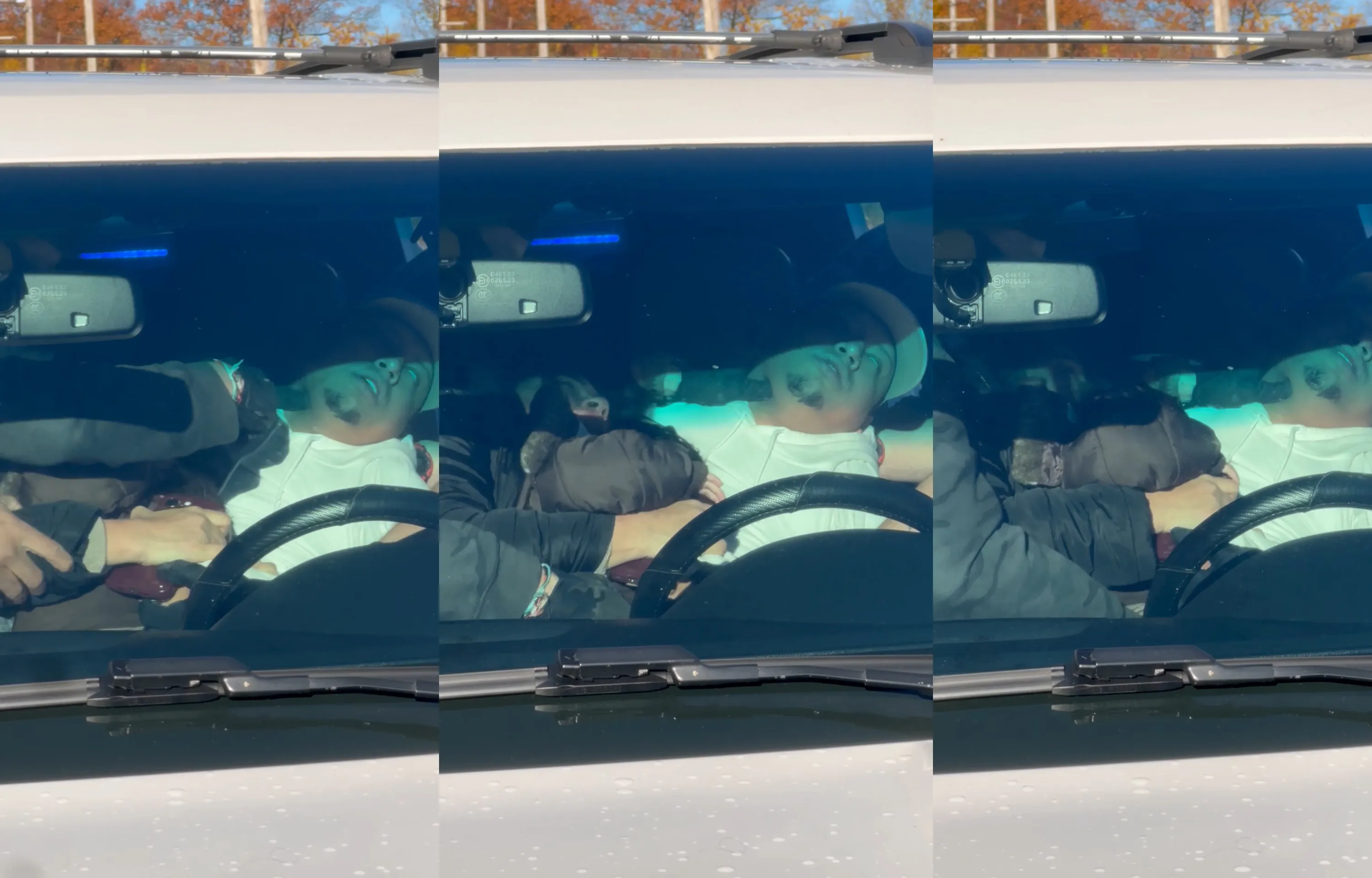 A man wearing a white shirt and baseball hat convulses in the driver’s seat of a car while a black-gloved hand presses into his neck.