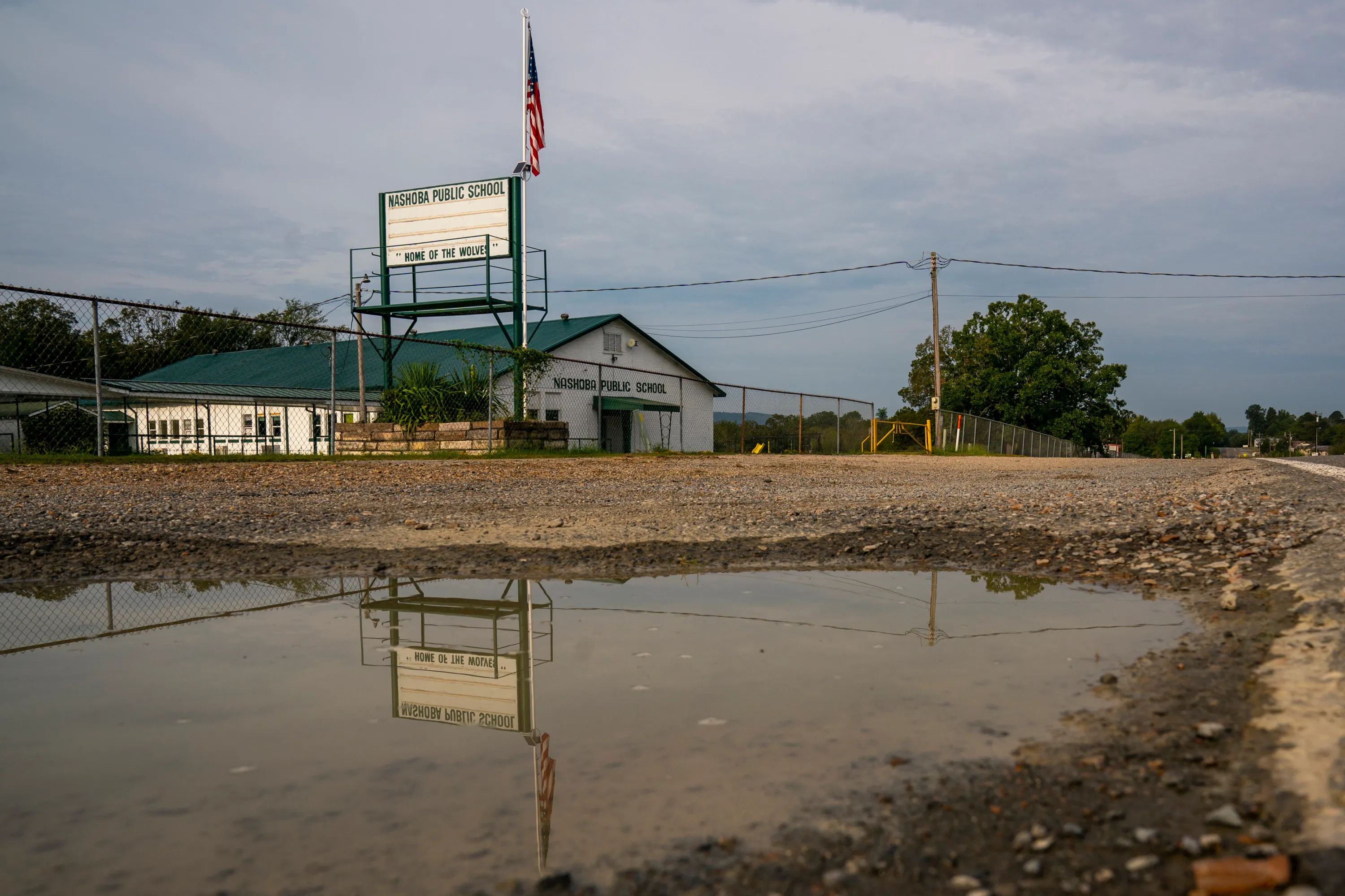 The Nashoba Public School marquee is seen reflected in a puddle alongside a rural road in Oklahoma.