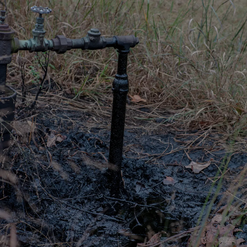An elbow of pipe with wet and blackened ground beneath it.