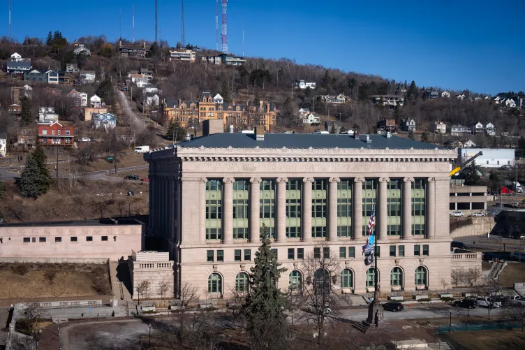 A large, tan courthouse with many residential houses on a hill rising behind it.