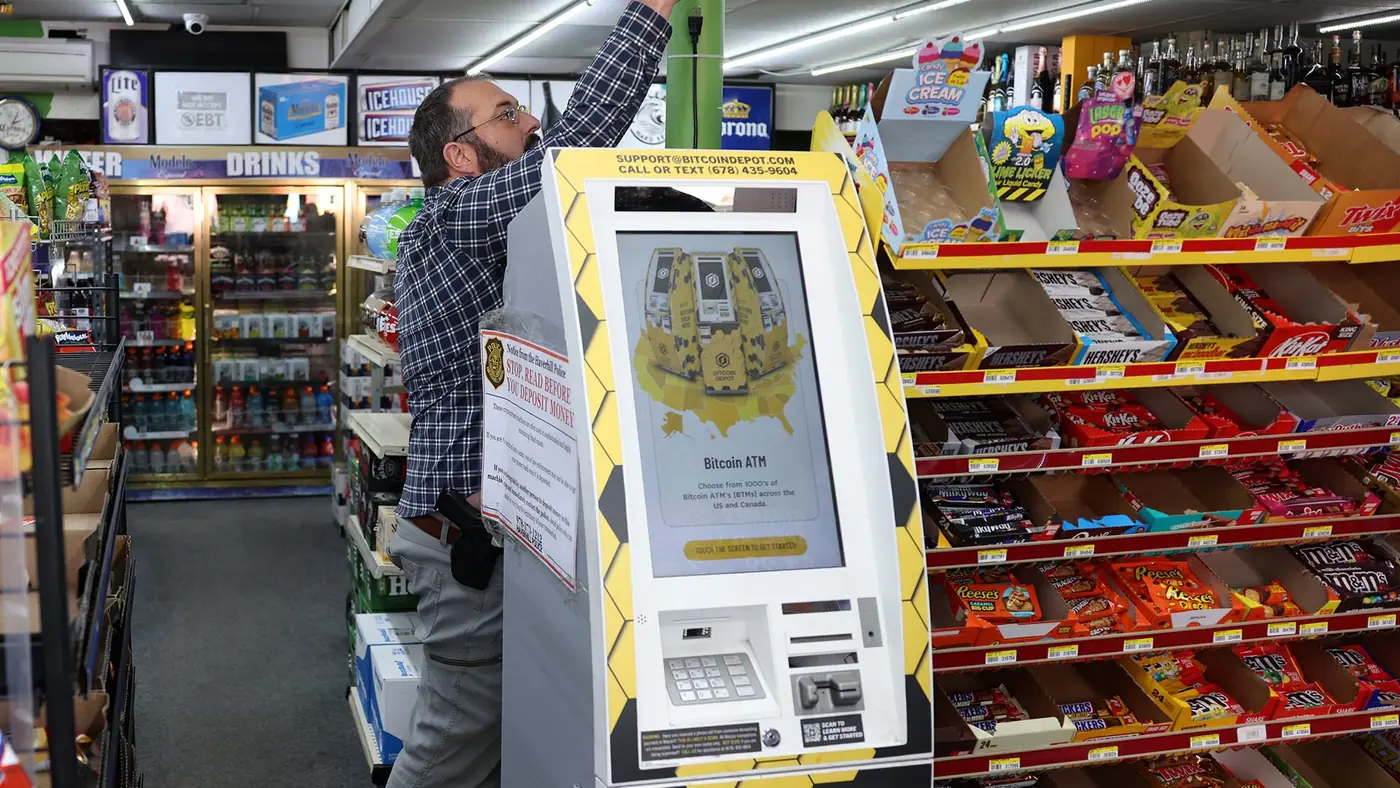 Photo of a Bitcoin Depot ATM in a convenience store with a man unplugging the machine.