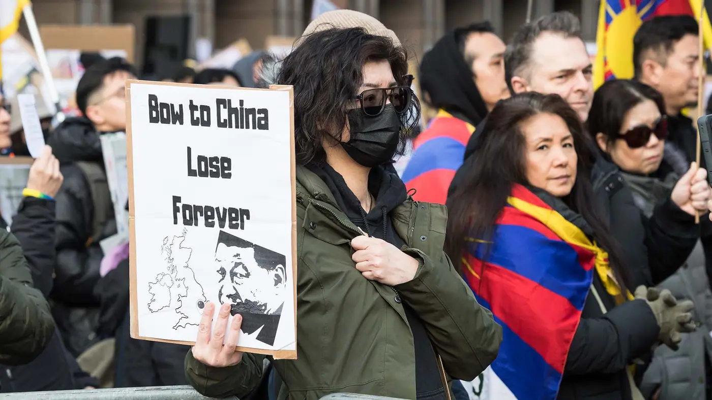 Photo of a group of protesters wearing flags and holding signs, including one that reads Bow to China Lose Forever.