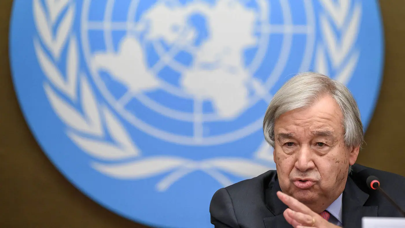 A man in a suit speaks into a microphone in front of the UN symbol