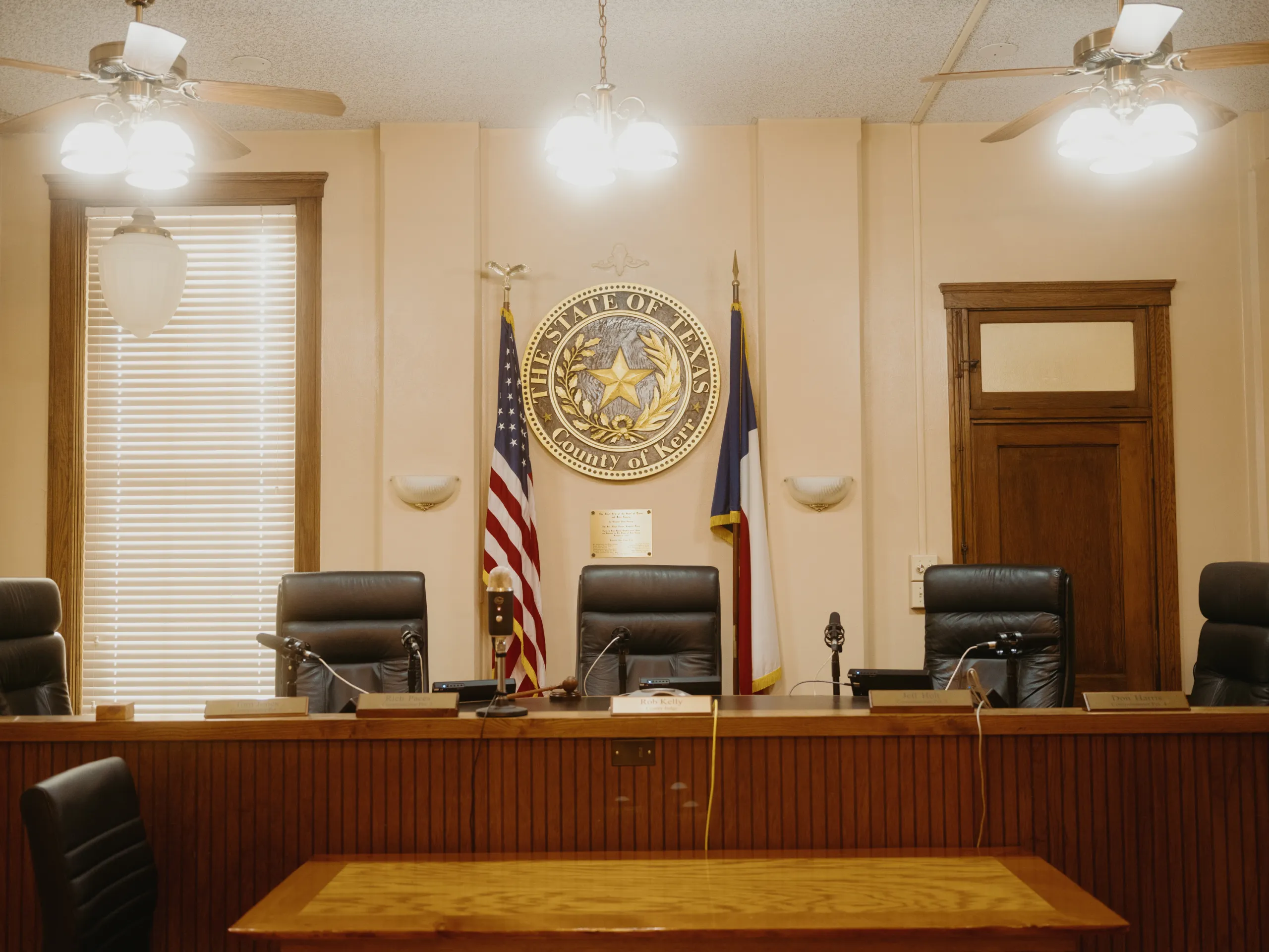 An empty courtroom with five large leather chairs behind the judge’s bench. An American flag and a Texas flag frame a large state seal on the wall.