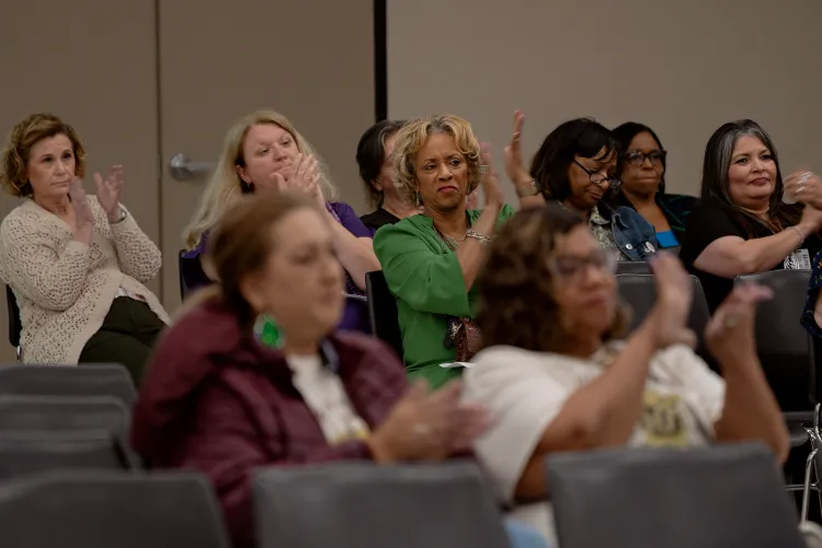 Women in rows of gray seats clap during a meeting.