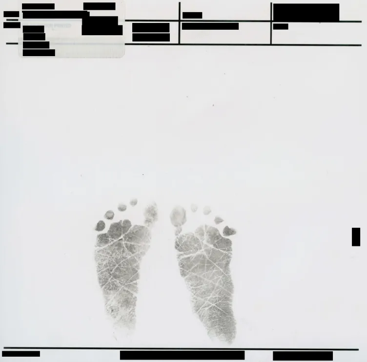 A pair of black ink footprints from an infant centered on a white page. Above and below the footprints are several rows of official form fields and identifying information, all of which have been redacted with solid black bars.