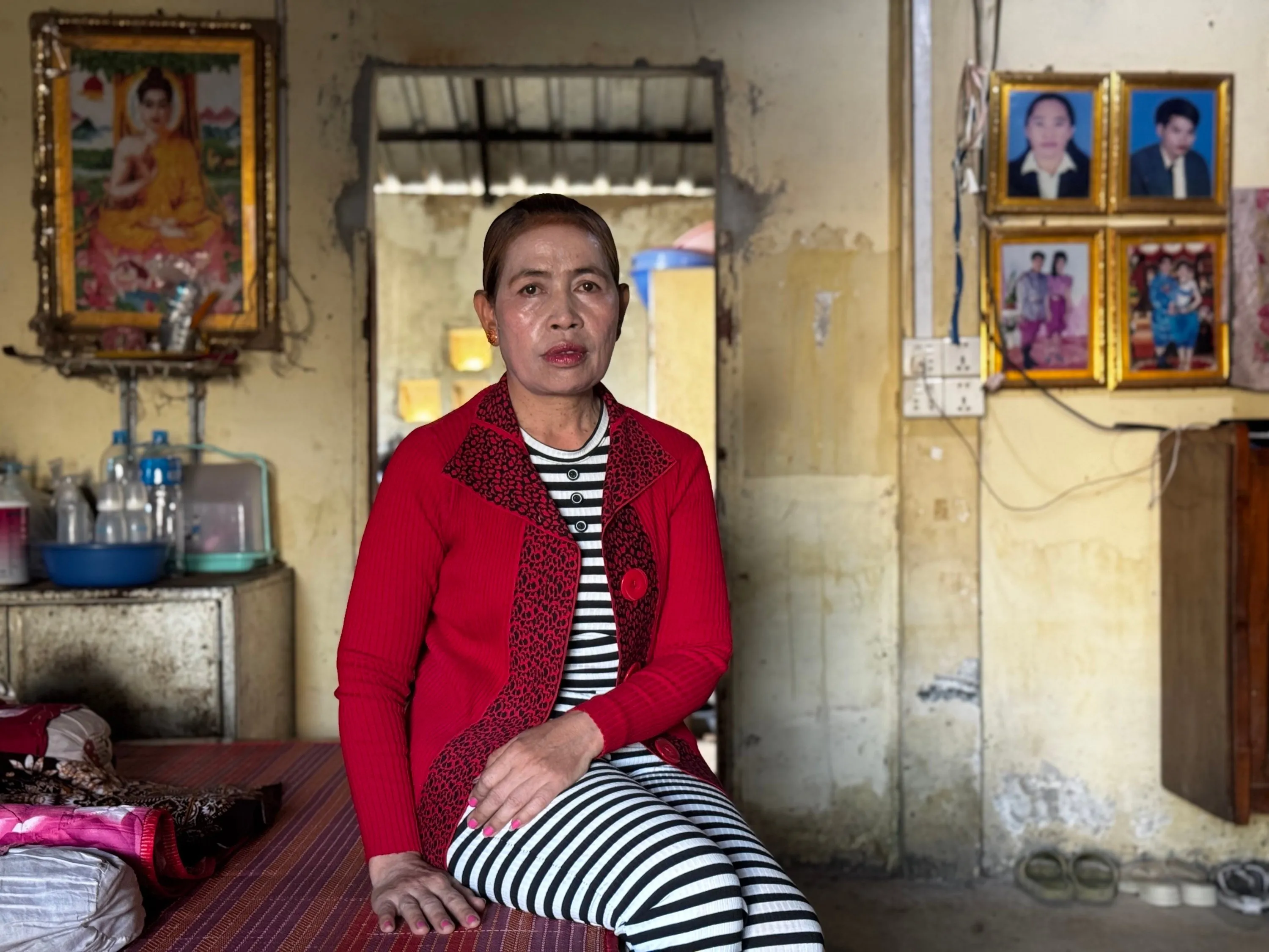 A woman wearing a red jacket over black-and-white-striped shirt and pants sits in a room with yellow walls and framed portraits.