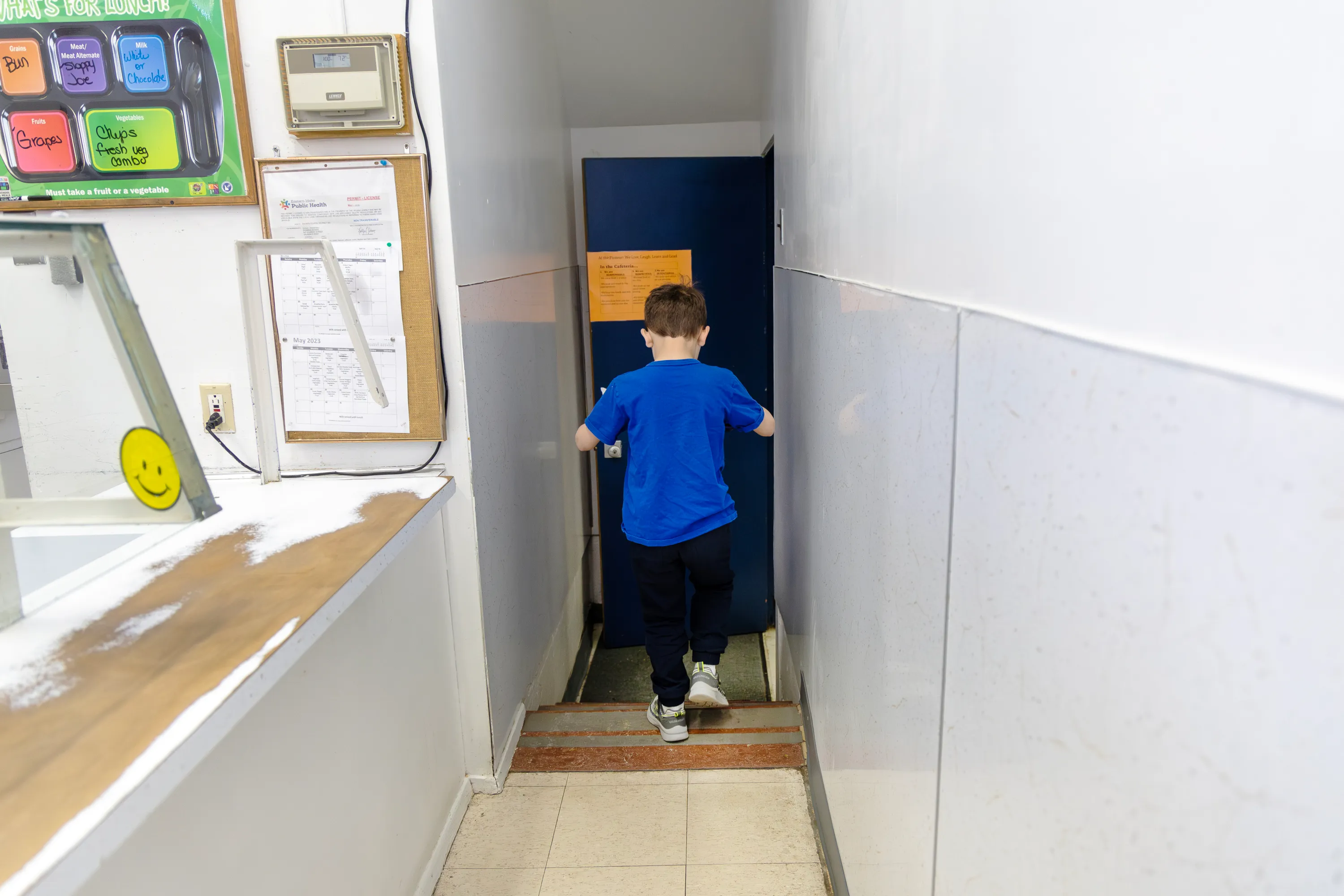 A young student walks down a stairway carrying his meal in a rural school cafeteria.