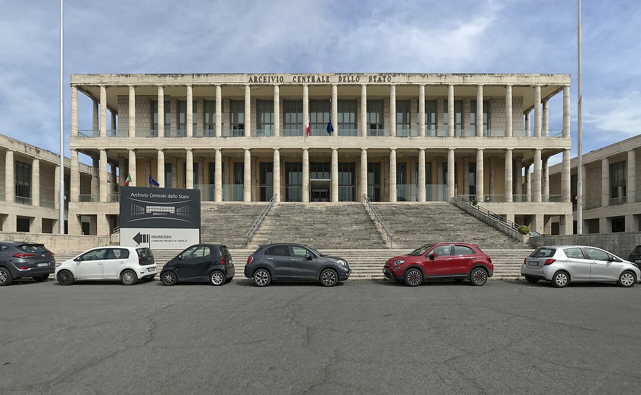La facciata colonnata dell'Archivio Centrale dello Stato con la scritta sul fregio, la grande scalinata d'ingresso e una fila di auto parcheggiate davanti