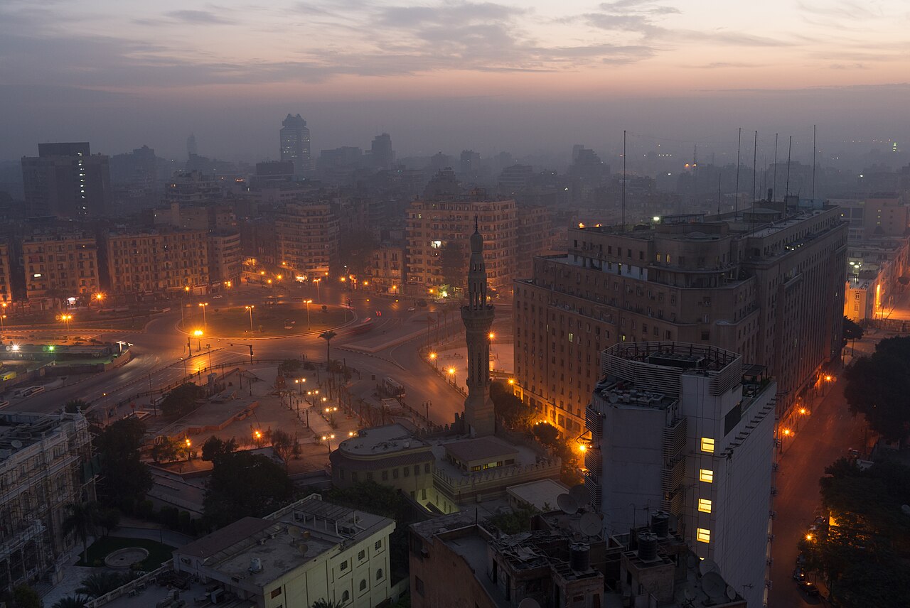 Piazza Tahrir al Cairo vista dall'alto alle prime luci del giorno, con i lampioni accesi, il minareto al centro, i palazzi intorno e il cielo arancione all'orizzonte