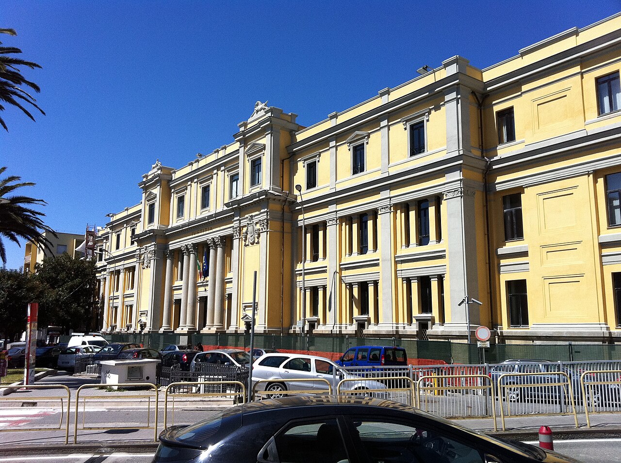 L'edificio giallo a più piani della Corte d'appello di Catanzaro, con colonne bianche all'ingresso, sotto un cielo azzurro, con auto parcheggiate davanti